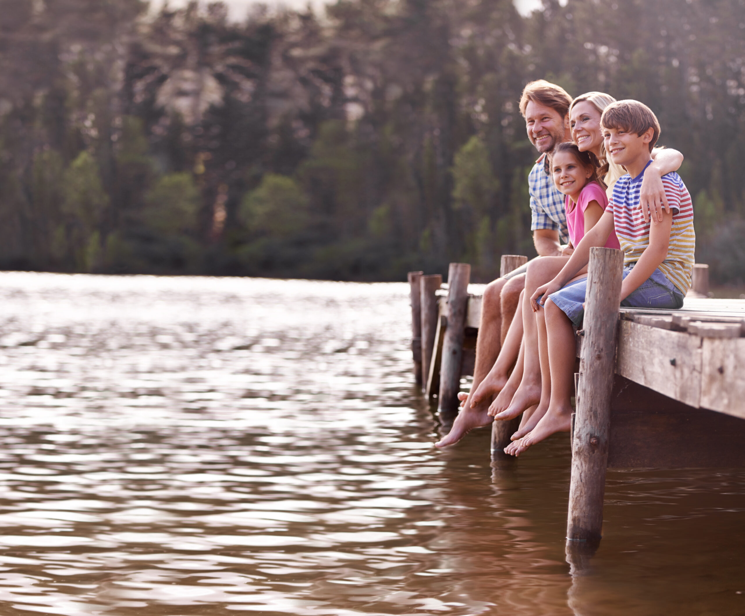 A happy family of four sitting on a jetty at the lake.