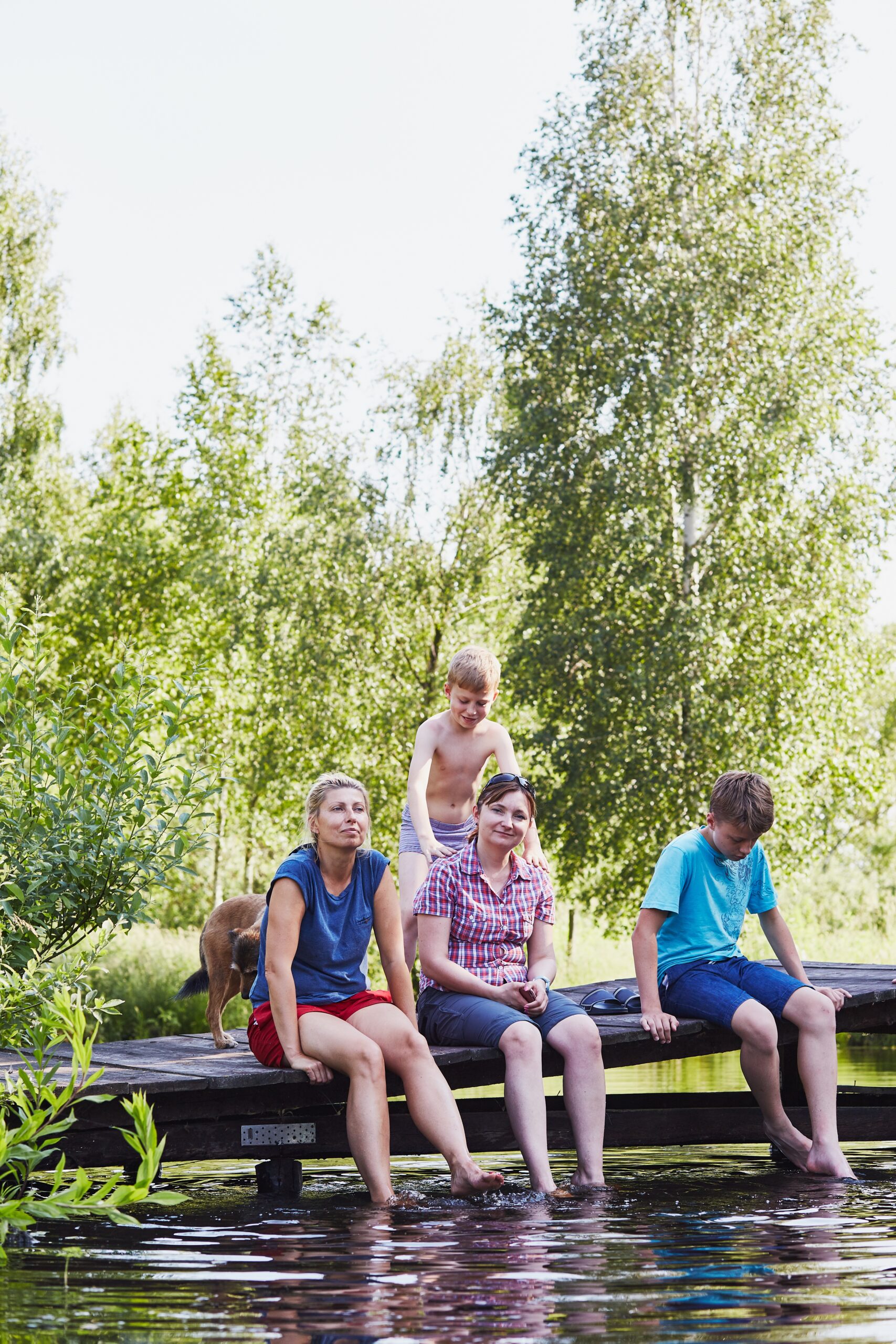 Family spending time together sitting on a bridge over a lake, among the trees, close to nature, during summer vacations. Candid people, real moments, authentic situations