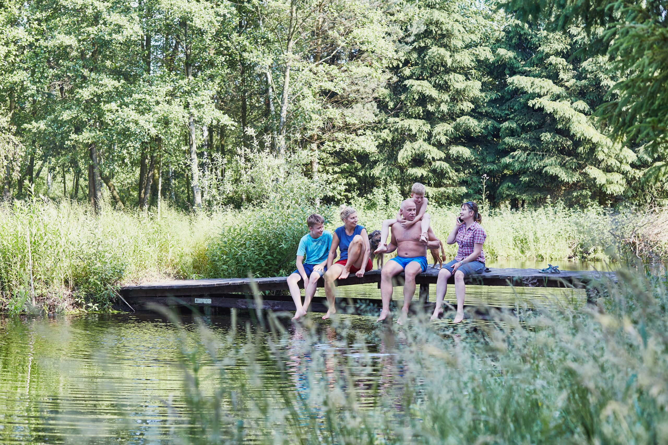 Family spending time together sitting on a bridge over a lake, among the trees, close to nature, during summer vacations. Candid people, real moments, authentic situations