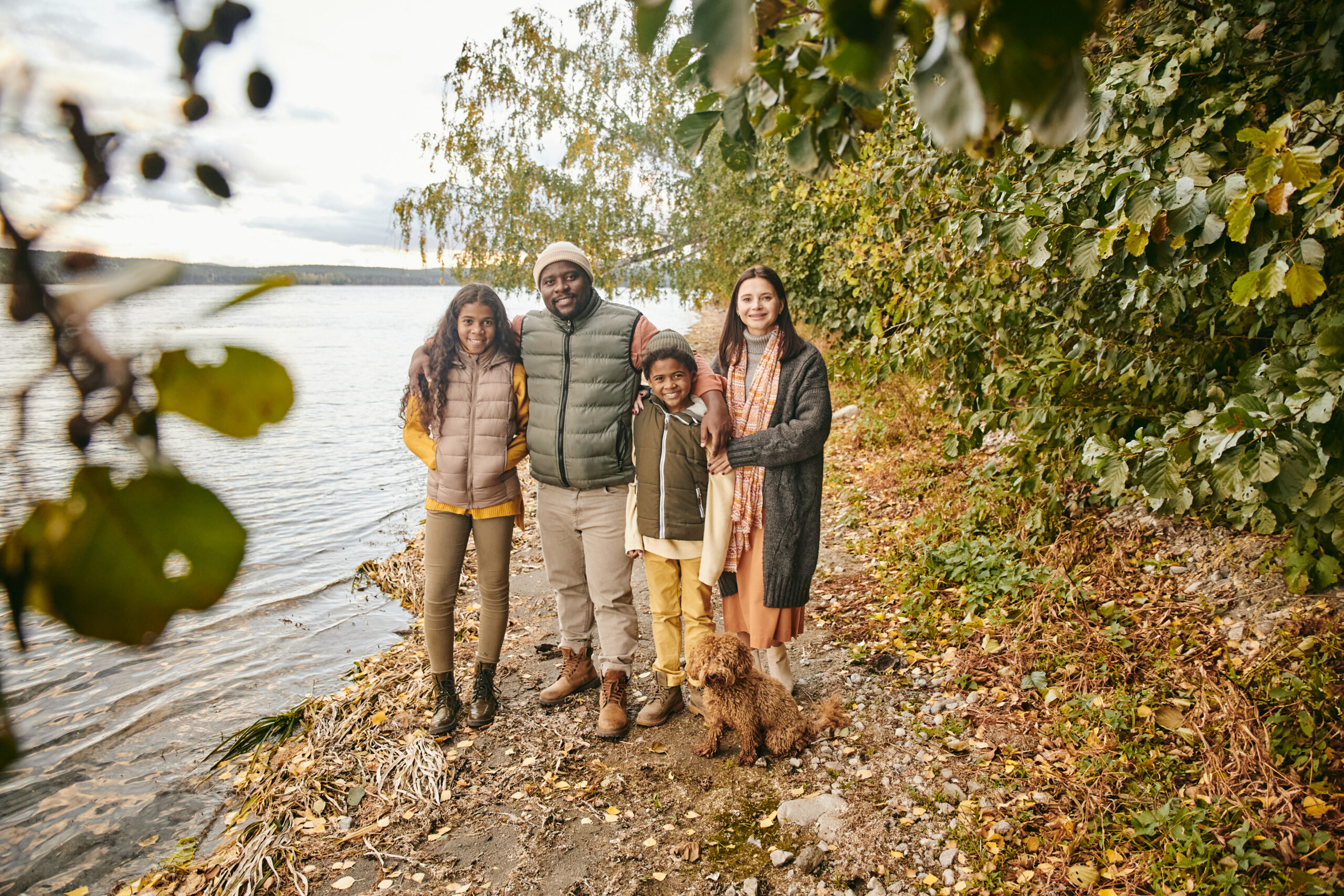 Portrait of happy family of four embracing and smiling at camera while walking together in autumn forest